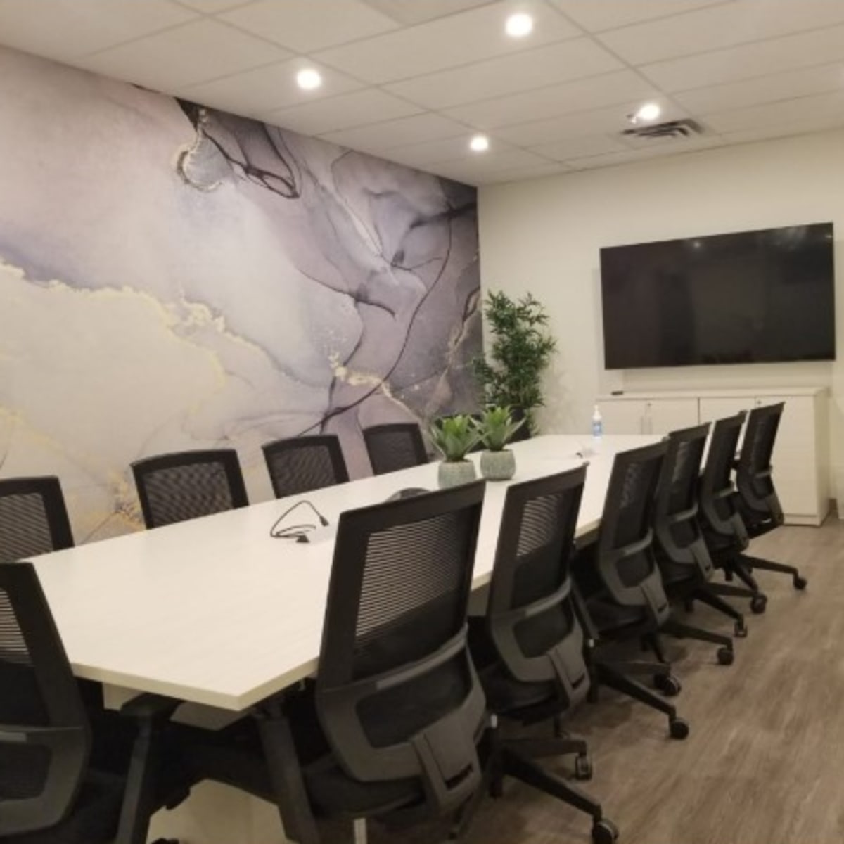 A modern conference room featuring a long white table surrounded by black ergonomic chairs, a large wall-mounted screen, and a decorative wall with abstract patterns.