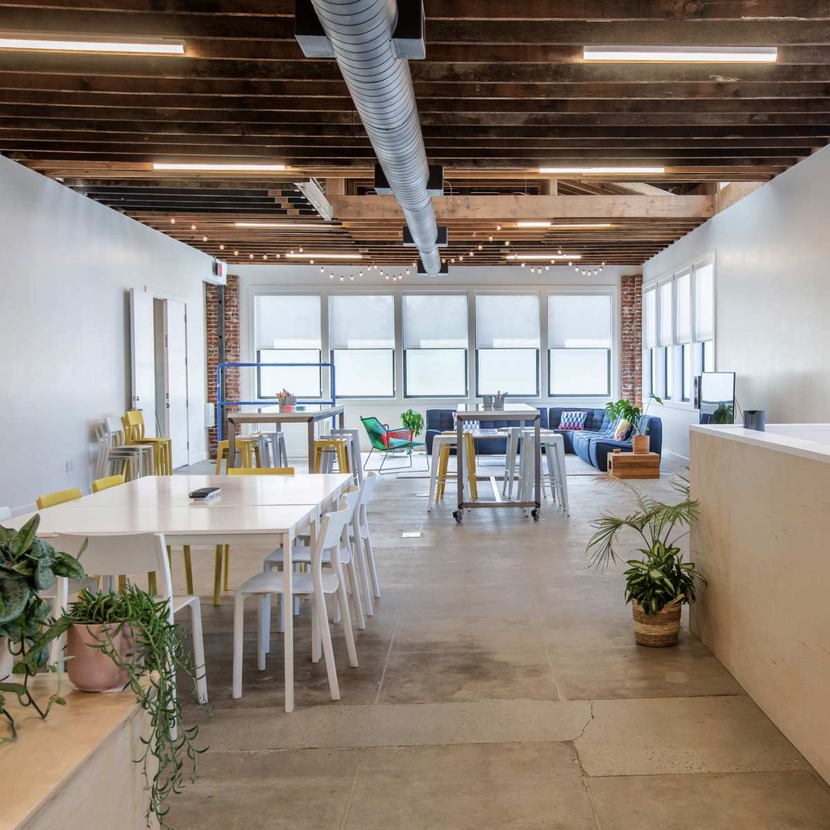 A spacious, modern open office area with a mix of seating arrangements, including tables and chairs, and large windows providing natural light.