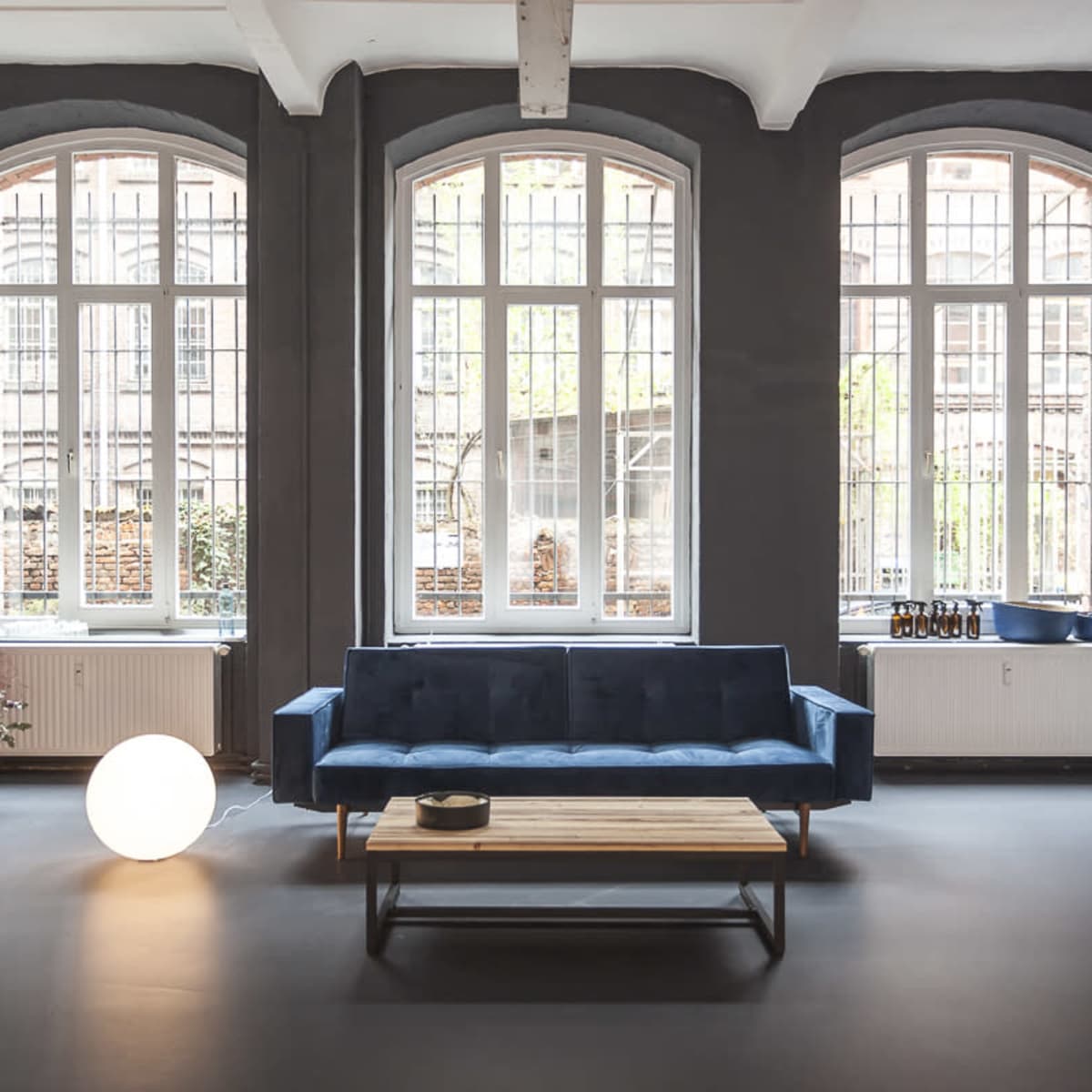 A modern, minimalist room features a blue sofa and a wooden coffee table, with large windows letting in natural light.