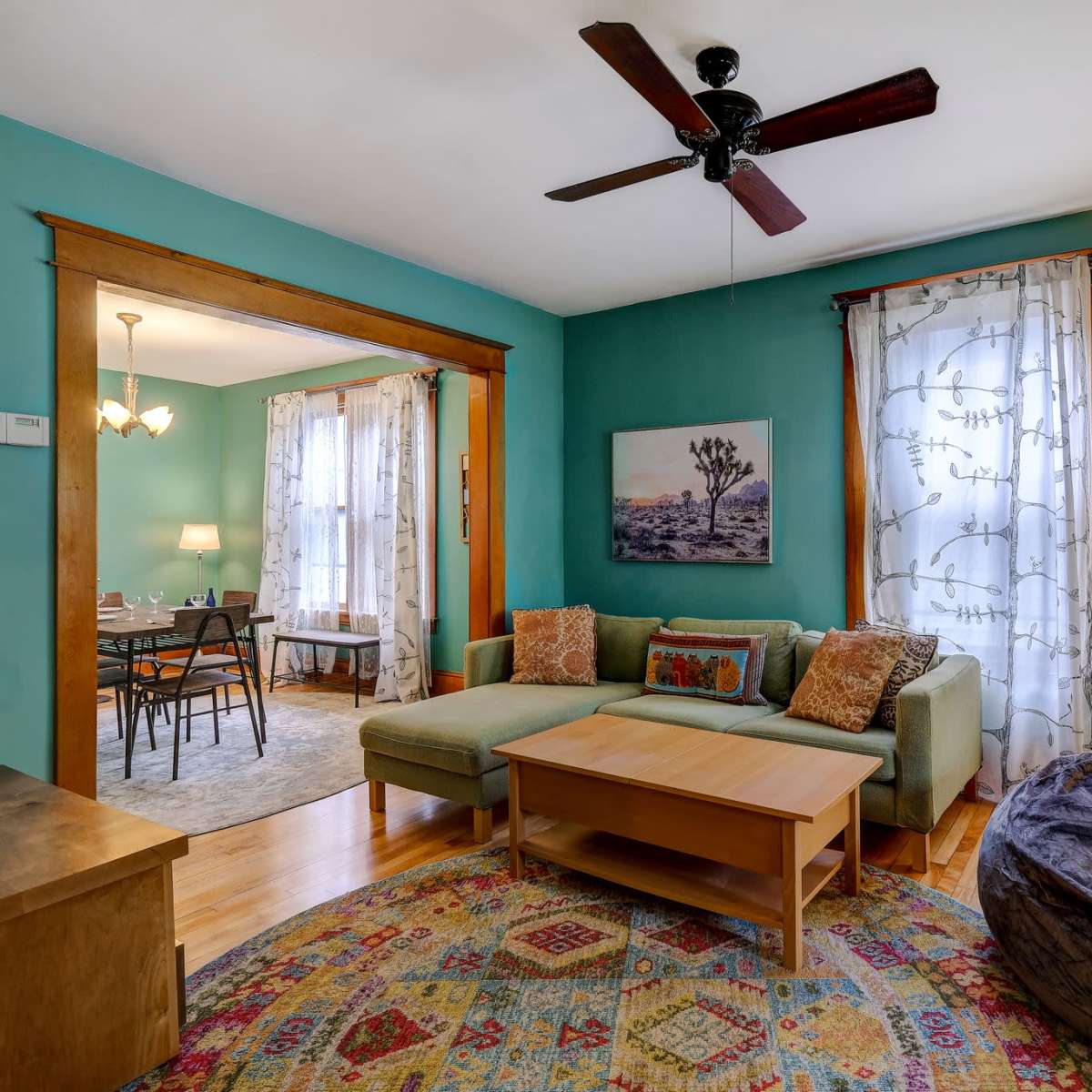 The room features a green-painted wall with a couch and a coffee table, framed by a doorway leading to a dining area.