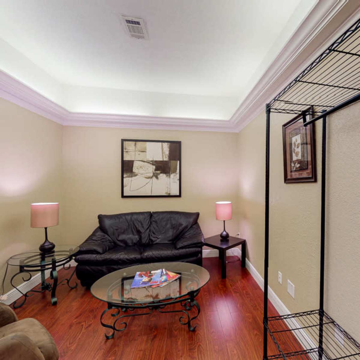 A small, neatly arranged room with a black leather couch, a glass coffee table, and two lamps providing soft lighting.