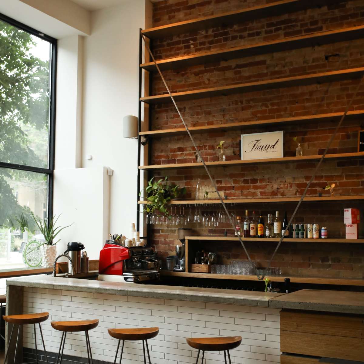 A modern coffee bar with a wooden counter, a brick wall, and four stool chairs in front of it.