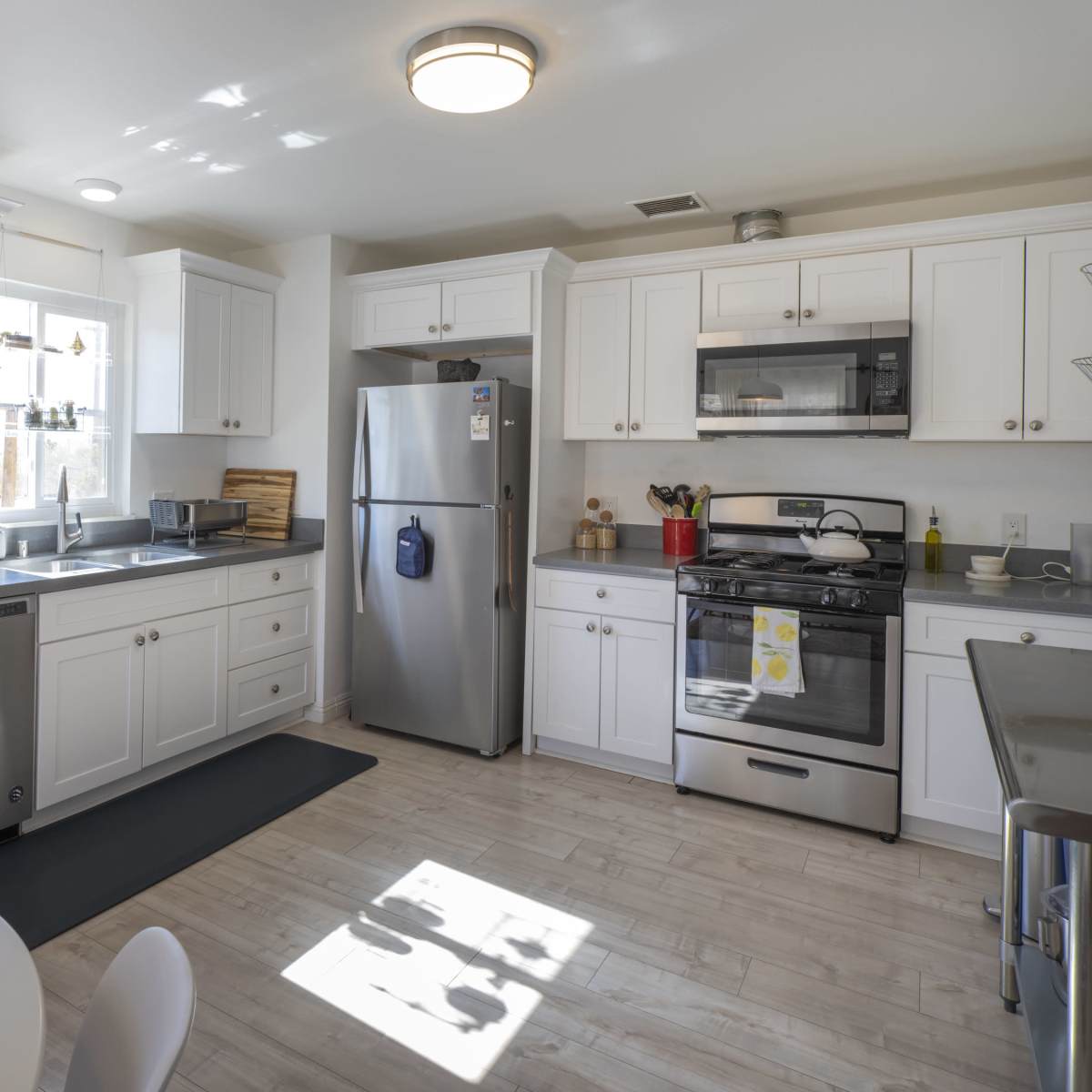 A modern kitchen features white cabinets, stainless steel appliances, and a gray countertop with a small dining table in the corner.