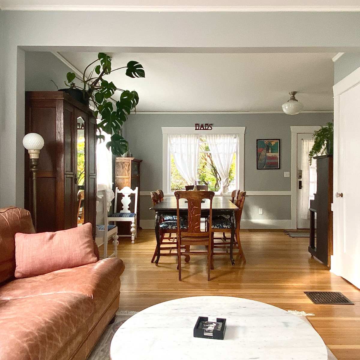 A cozy living room features a brown leather sofa and a marble coffee table, with a dining area visible in the background.