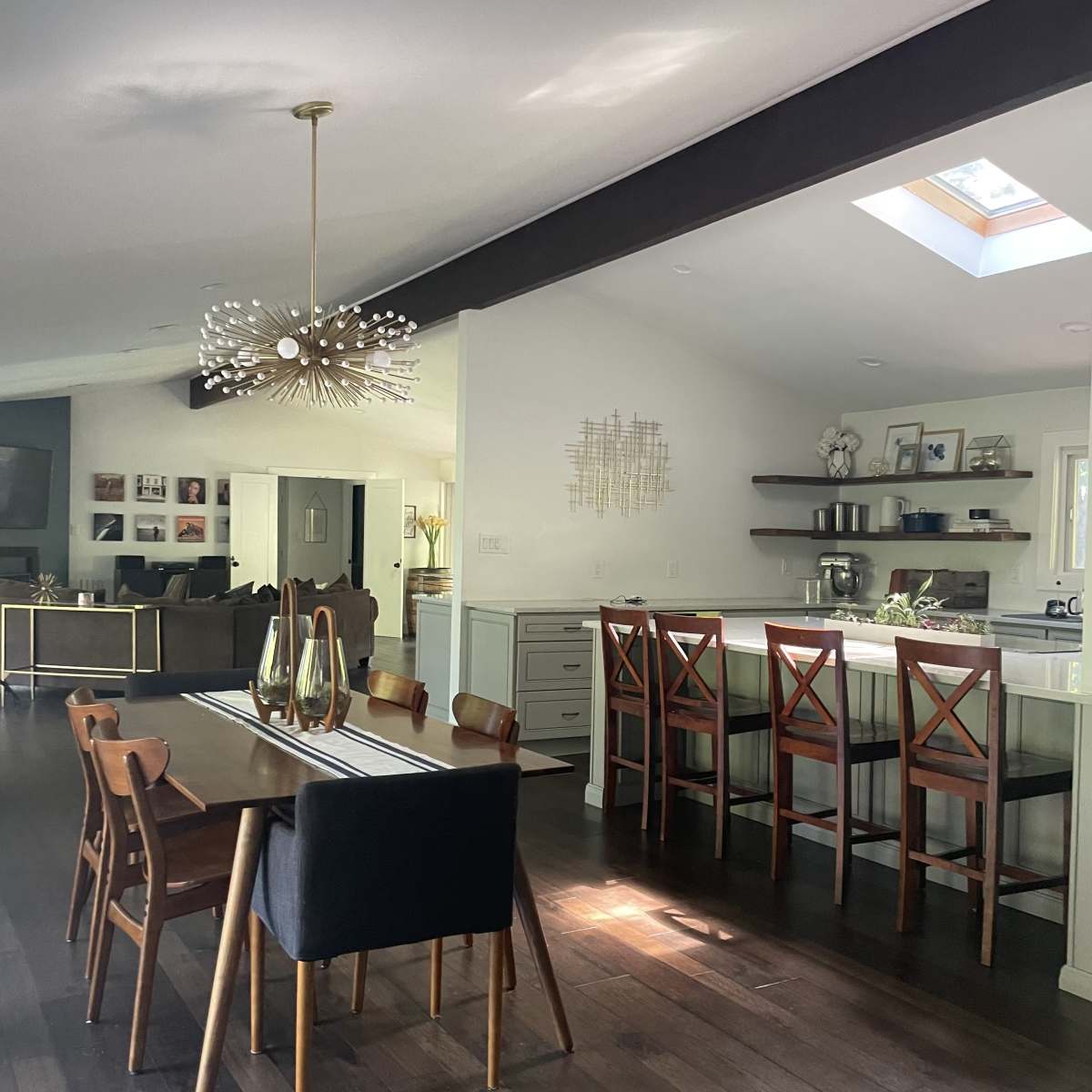 A dining area with a wooden table and chairs is adjacent to a kitchen with bar seating, all illuminated by natural light through a skylight.