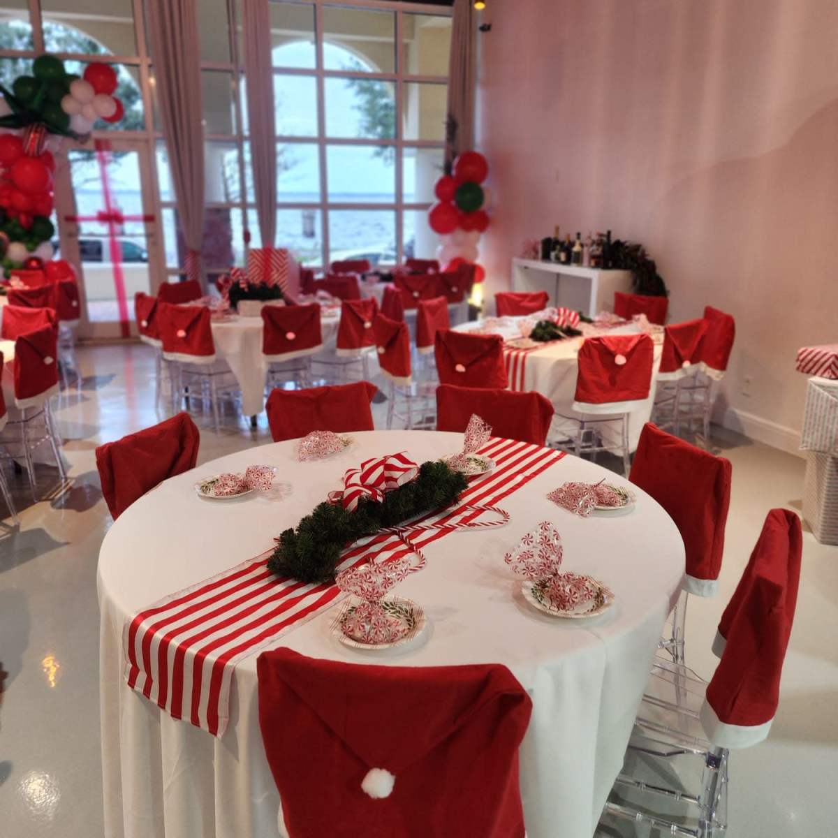 A festive dining area decorated with red and white table settings, including Santa hat accents on the chairs and holiday-themed centerpieces.