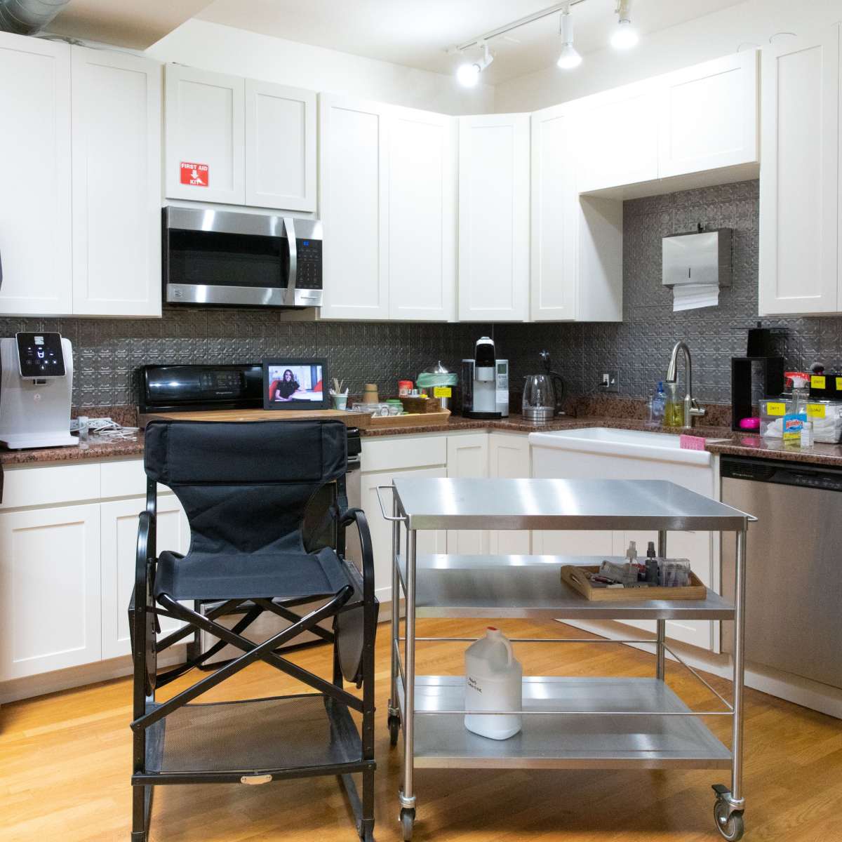A modern kitchen with white cabinets, stainless steel appliances, and a folding chair next to a metal serving cart.