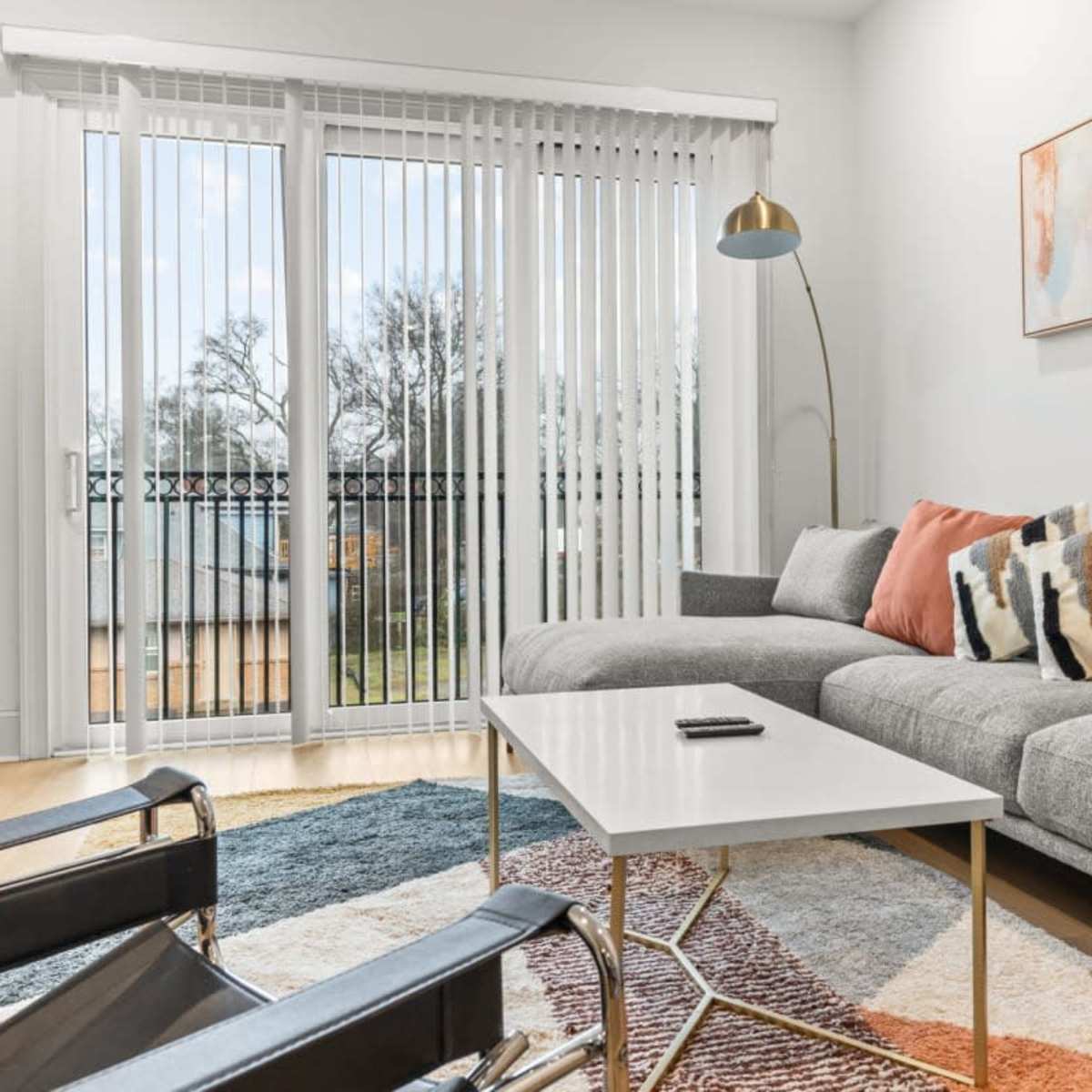 A modern living room with a gray sectional sofa, a white coffee table, and large windows draped with vertical blinds.