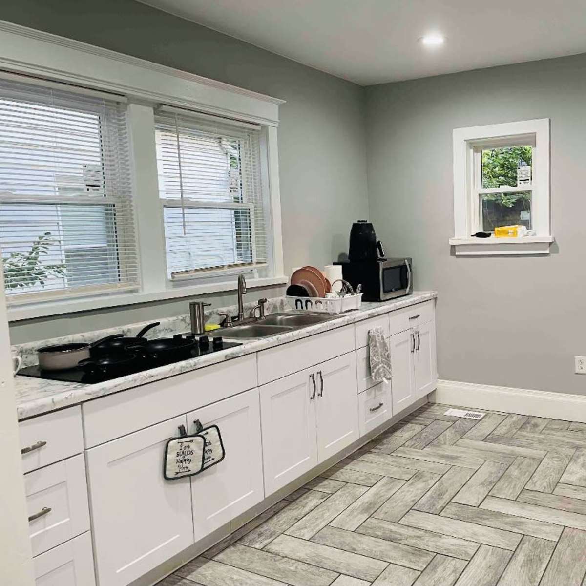 The kitchen features white cabinetry, a large stainless steel refrigerator, and a light gray color scheme with a herringbone patterned floor.