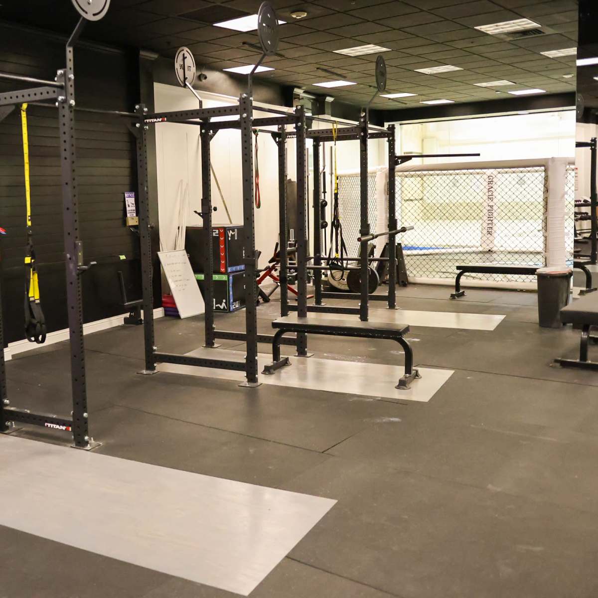 A gym interior with multiple squat racks and exercise equipment on a rubber flooring surface.
