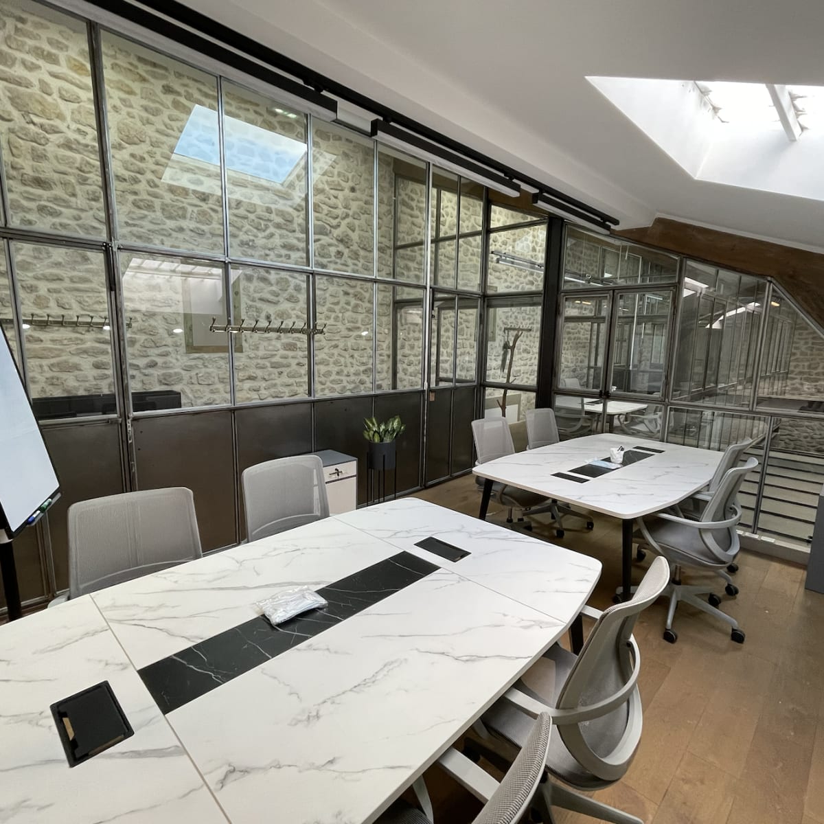 A modern conference room features a long marble table, sleek chairs, and glass walls showcasing a stone interior.