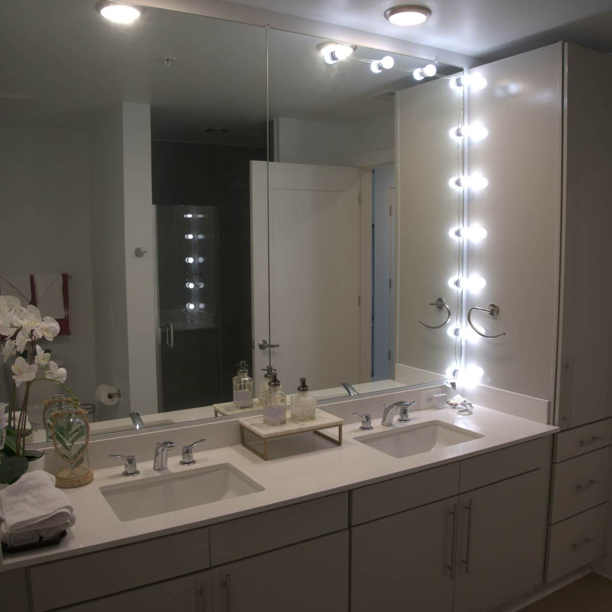 A modern bathroom with a double vanity, large mirrors, and bright LED lighting.
