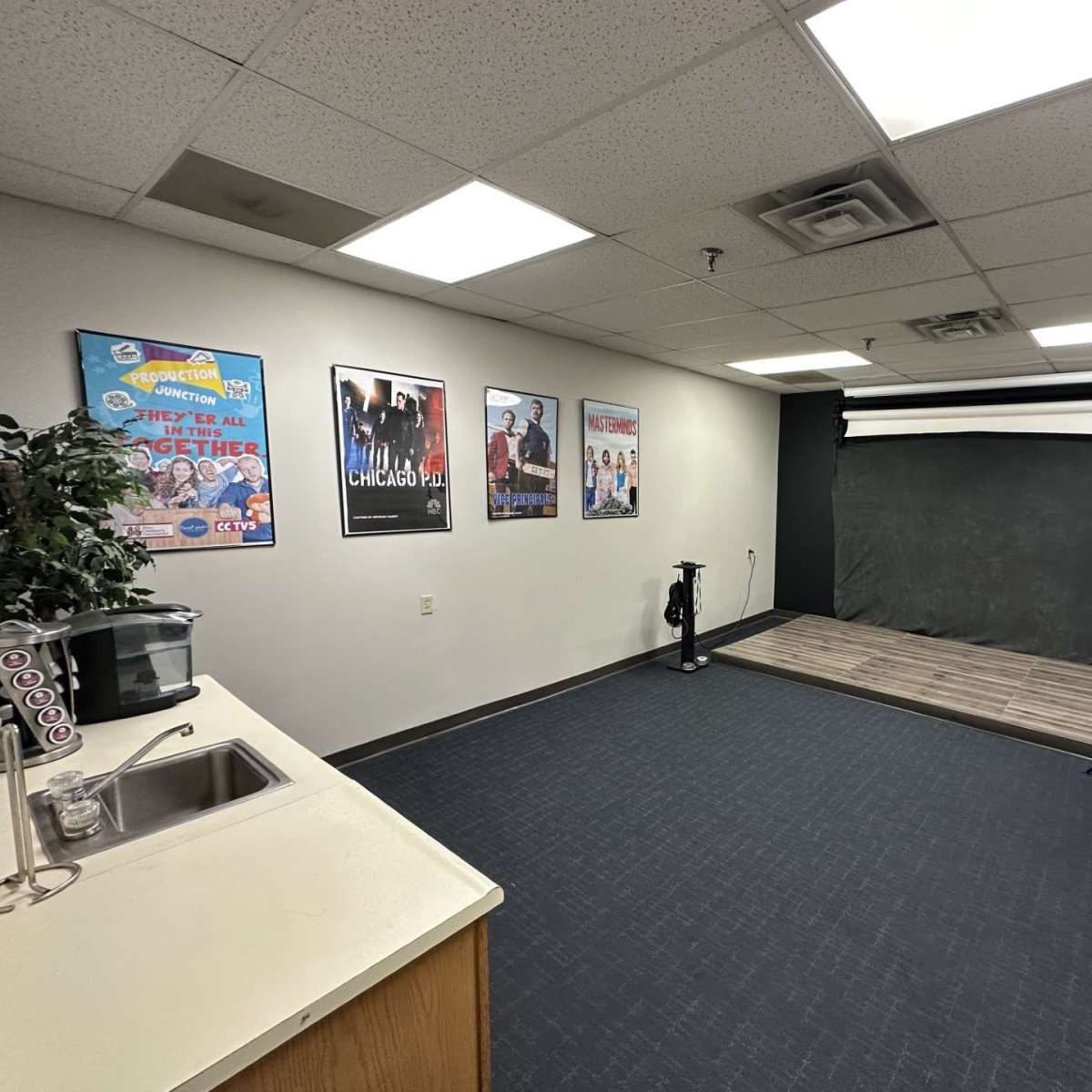 A spacious room featuring a kitchenette, promotional movie posters on the walls, and a photography backdrop with lighting equipment set up in the corner.