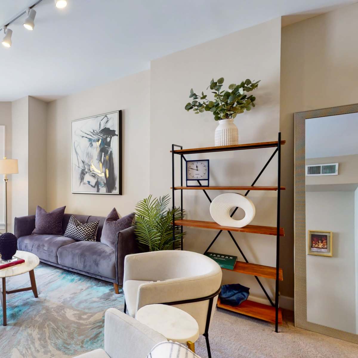 A modern living room featuring a gray sofa, a round coffee table, a decorative shelving unit, and large windows allowing natural light.