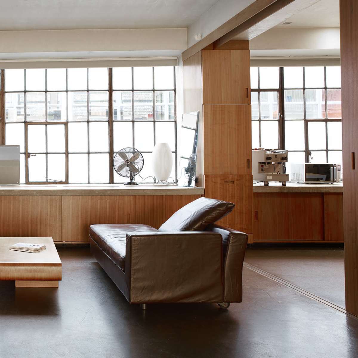 A modern living area features two leather sofas facing a wooden coffee table, with large windows providing natural light.