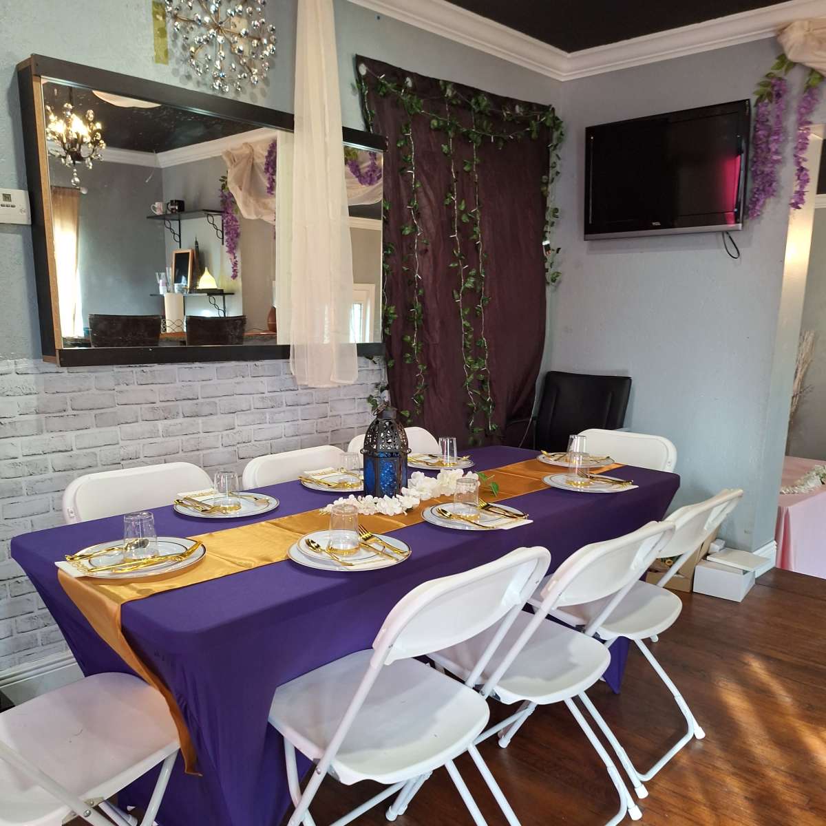 A dining table set with a purple tablecloth and gold accents is arranged with white chairs in a decorated indoor space.