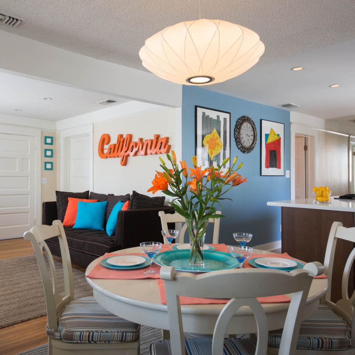 A bright and modern living space features a dining area with a round white table set for four, surrounded by colorful decor and a cozy sofa.