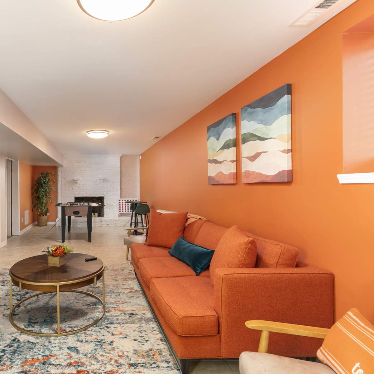 A modern living room with an orange accent wall, a large flat-screen TV mounted on one wall, a comfortable orange sofa, and artwork above the sofa.