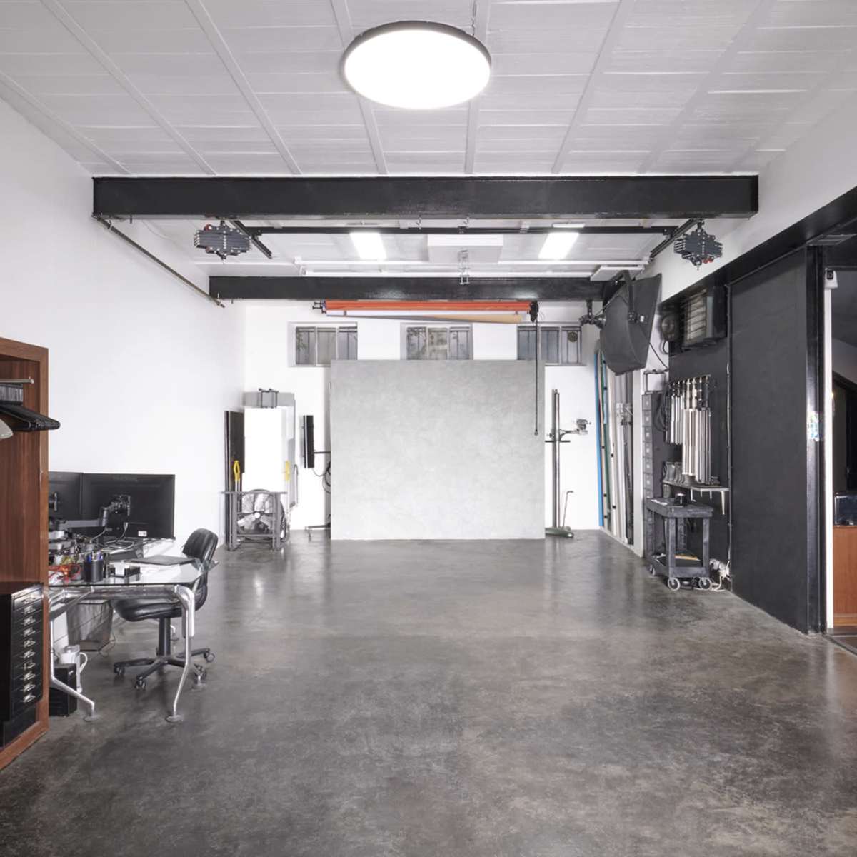 A spacious, well-lit studio with a gray backdrop, a black office chair, and a clothing rack against one wall.