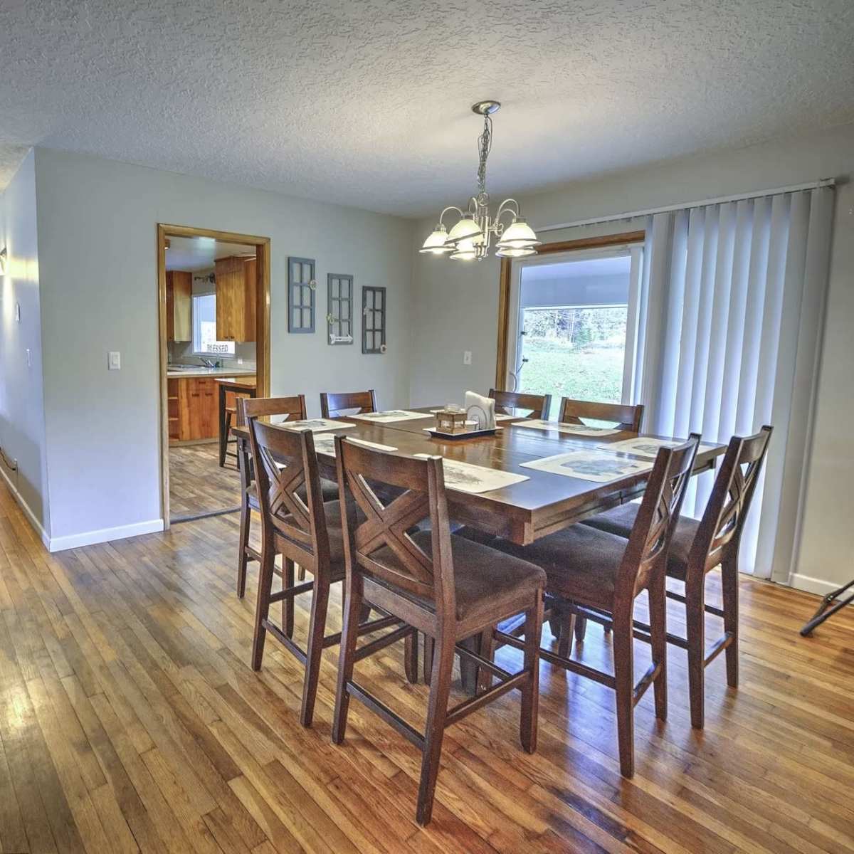 A spacious dining area with a wooden table and chairs, adjacent to a kitchen and a hallway with hardwood flooring.