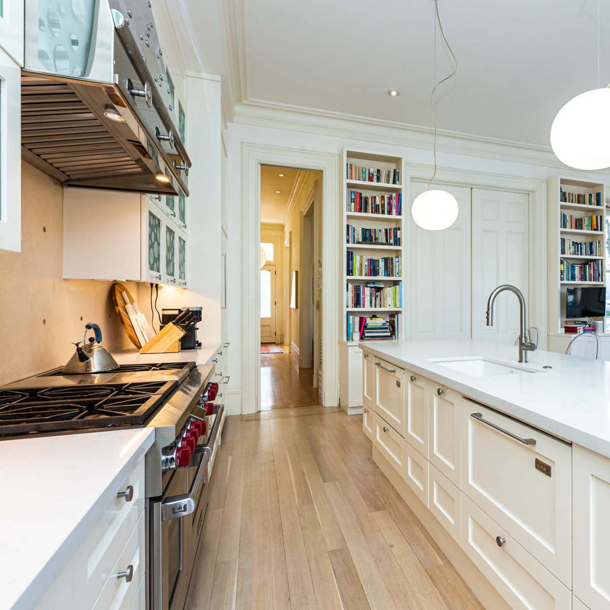 A modern kitchen features a central island with a white countertop, stainless steel appliances, and bookshelves in the background.