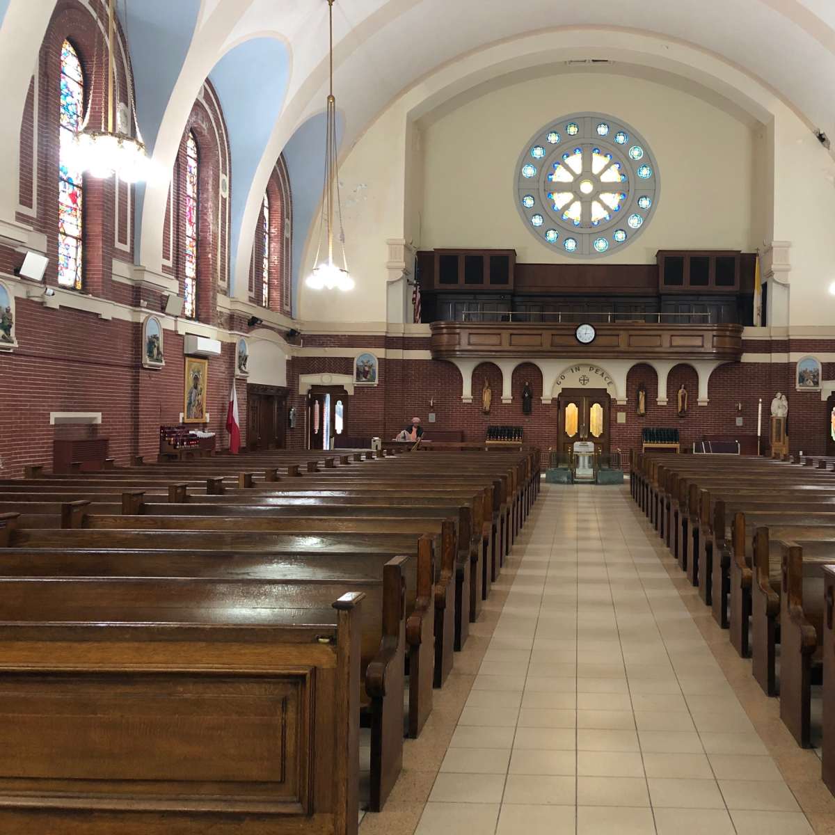 The interior of a large church with wooden pews arranged in rows and a circular stained glass window at the far end.