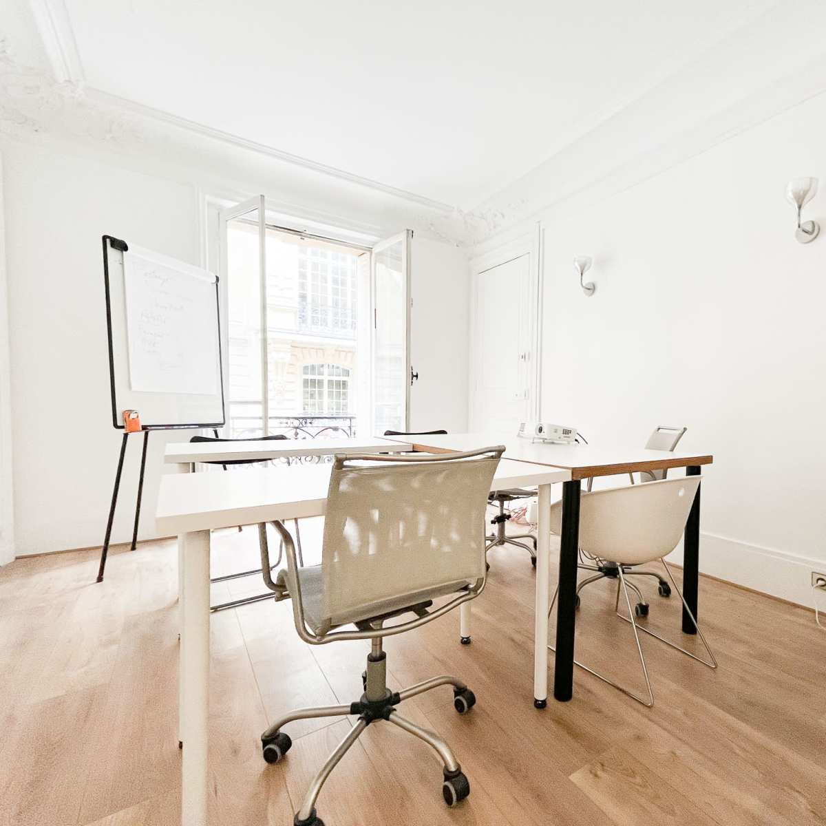 A bright, minimalist office space with a table and several chairs, and large windows opening to an outdoor view.