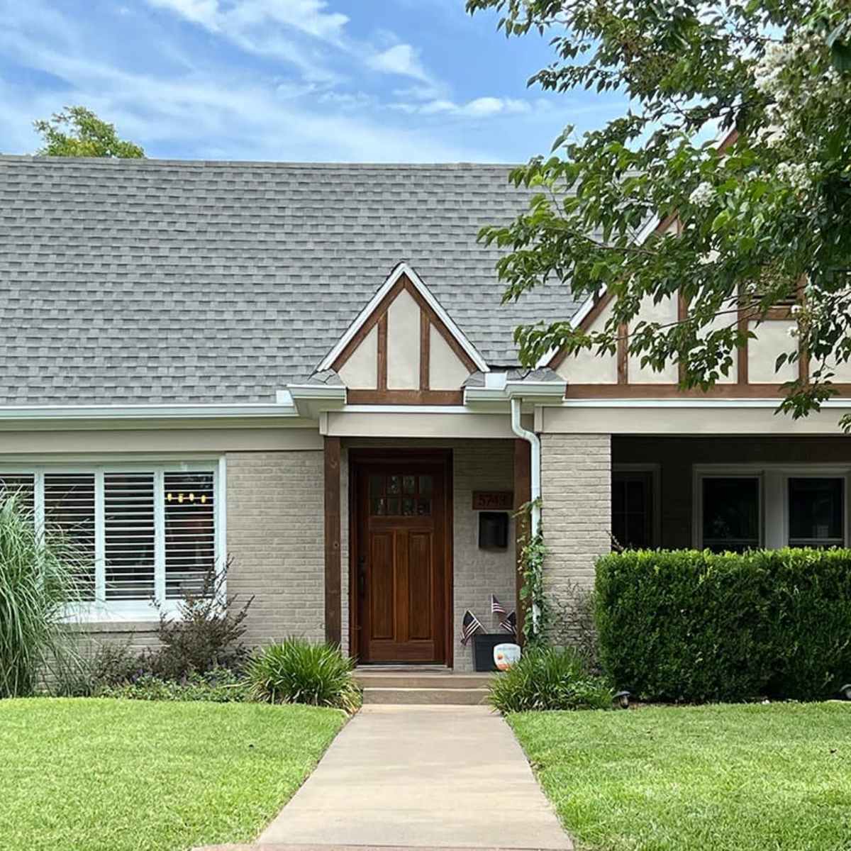 A two-story house with a steeply pitched roof features a brick facade and decorative timber accents.