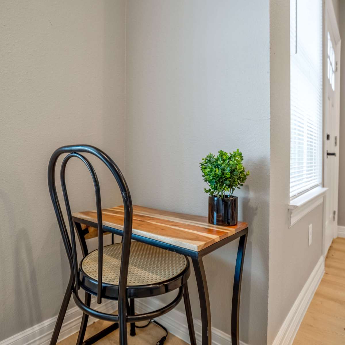 A small wooden table with a black chair and a potted plant sits in a corner near a window.
