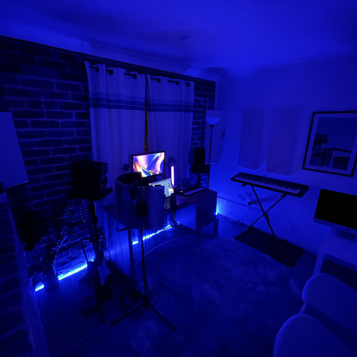 A dimly lit room with blue lighting, featuring music equipment, a computer, and a keyboard against a brick wall.