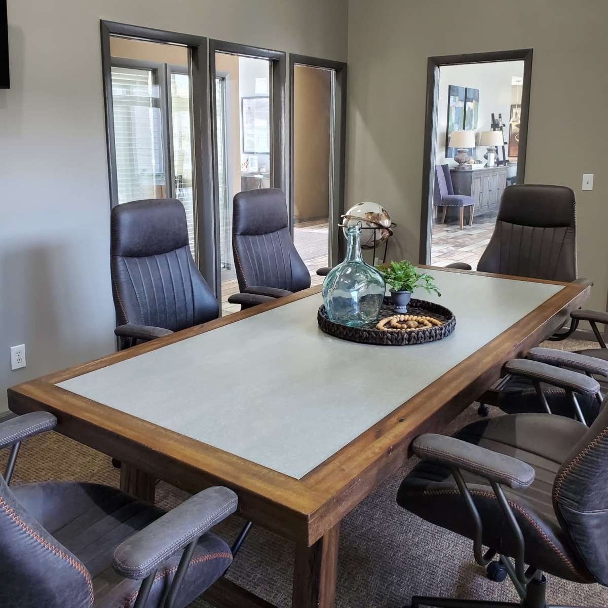 A conference room features a wooden table surrounded by ergonomic chairs and three mirrors reflecting the space.