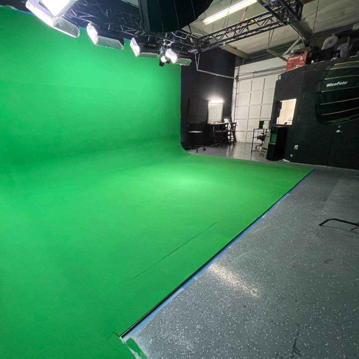An empty green screen studio with overhead lights and a polished floor.