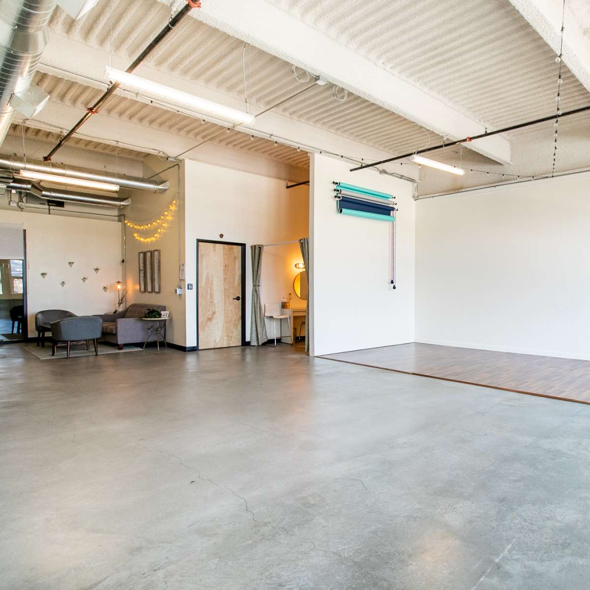 A spacious interior room with concrete flooring, a small seating area, and large windows allowing natural light to enter.