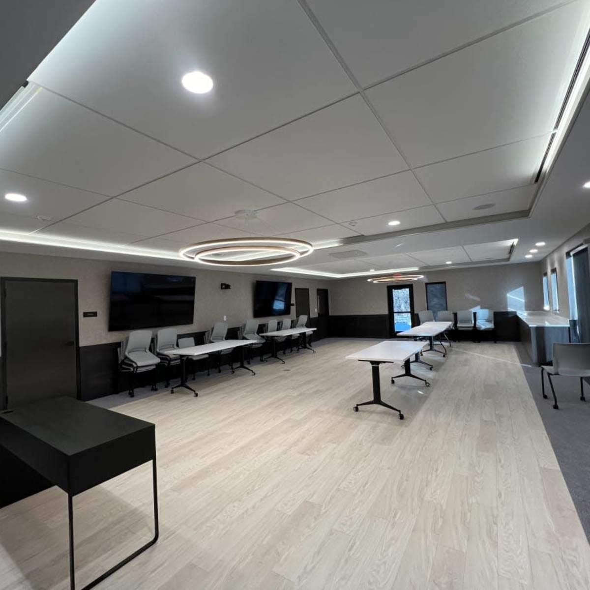 A modern conference room equipped with multiple tables, chairs, and wall-mounted screens.