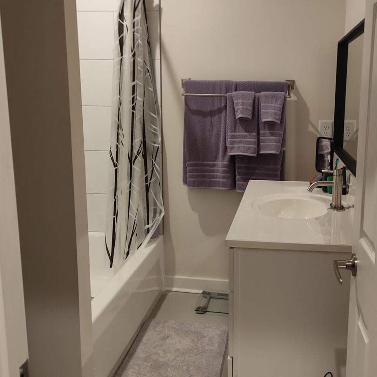 A small bathroom featuring a bathtub, a sink with a mirror, and towels hanging on the wall.