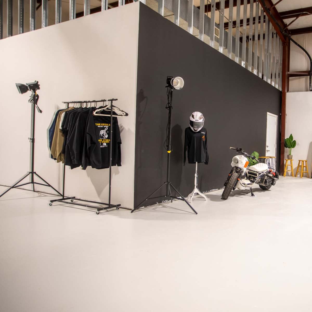 An industrial space with a black wall, clothing racks, a motorcycle, and various lighting equipment.