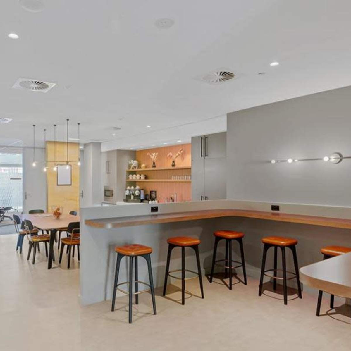 A spacious, modern café features a minimalist design with a wooden bar, high stools, and a variety of seating options.