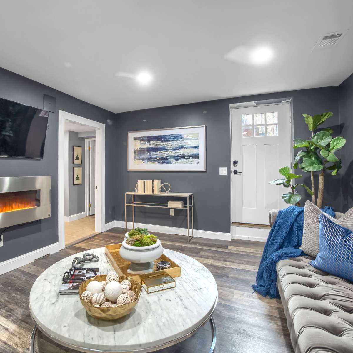 A modern living room with a mounted flat-screen TV, a contemporary fireplace, a round coffee table, and a door leading outside.