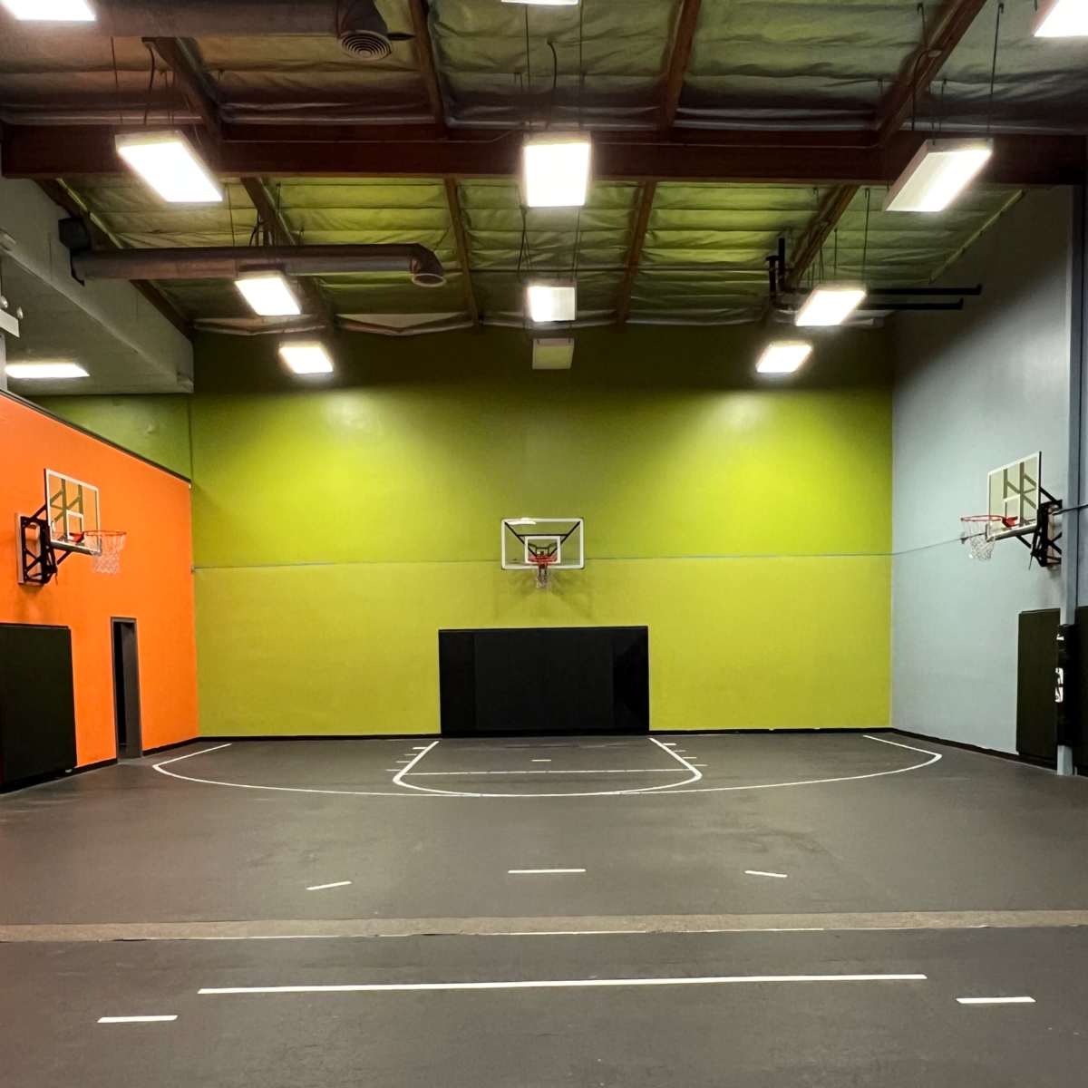 An indoor basketball court with two hoops and brightly colored walls in orange and green.