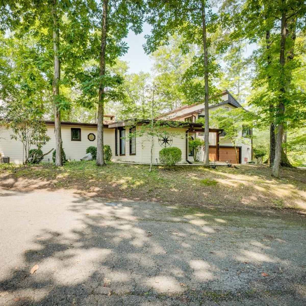 A single-story house is situated among trees, with a driveway leading up to it.