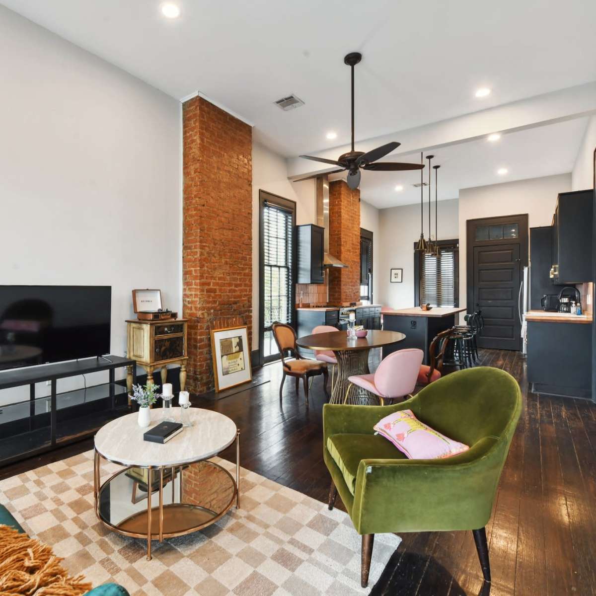 A modern living room with a green sofa, a circular coffee table, a television on a stand, and a dining area featuring a kitchen in the background.