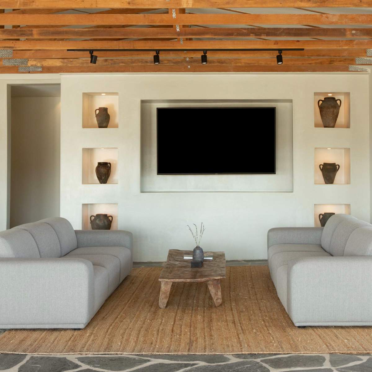 A modern living room with two gray couches facing a wooden coffee table on a textured stone floor, set against a wall featuring built-in shelves with decorative vases.