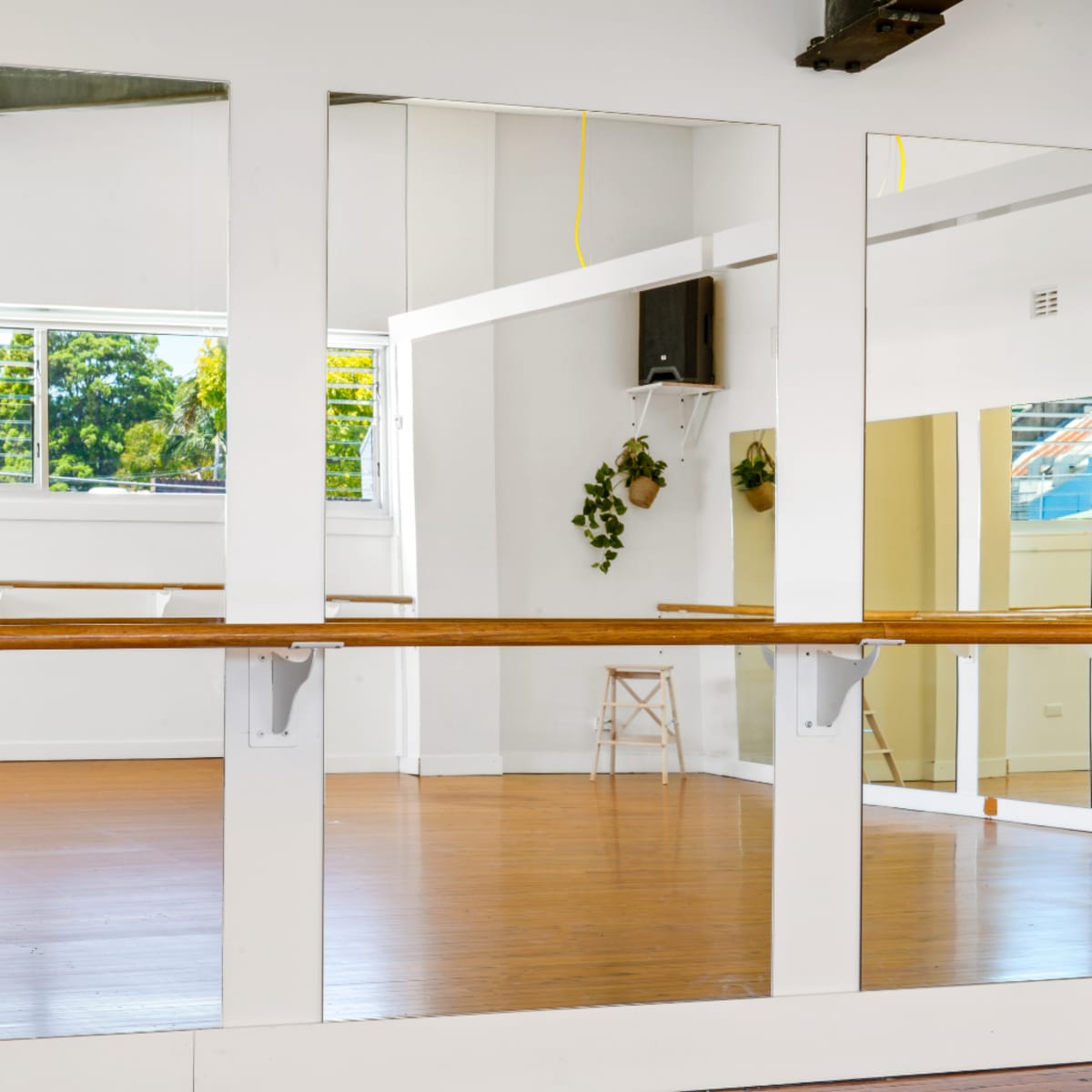 A bright dance studio with large mirrors, wooden flooring, and natural light coming through windows.