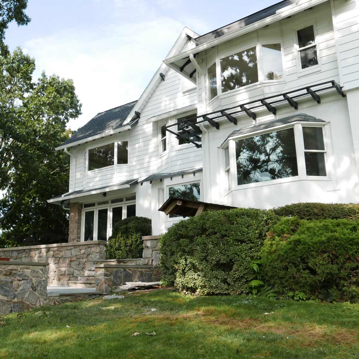 A multi-story house with white siding and stone accents is set on a landscaped yard with green grass and trees.