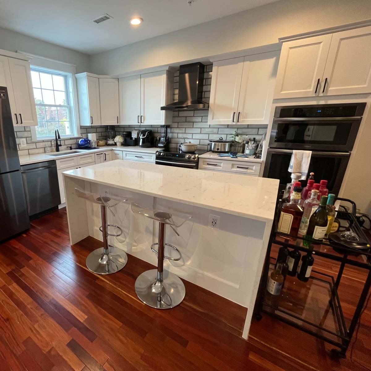 A modern kitchen with white cabinets, stainless steel appliances, and a central island equipped with two clear bar stools.
