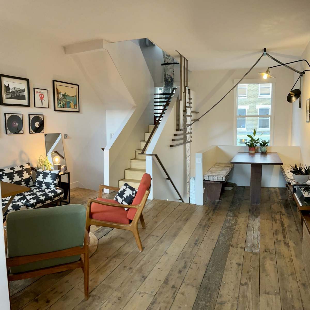 A cozy living space with a dining area, a staircase, and artwork on the walls, featuring wooden floors and various seating options.