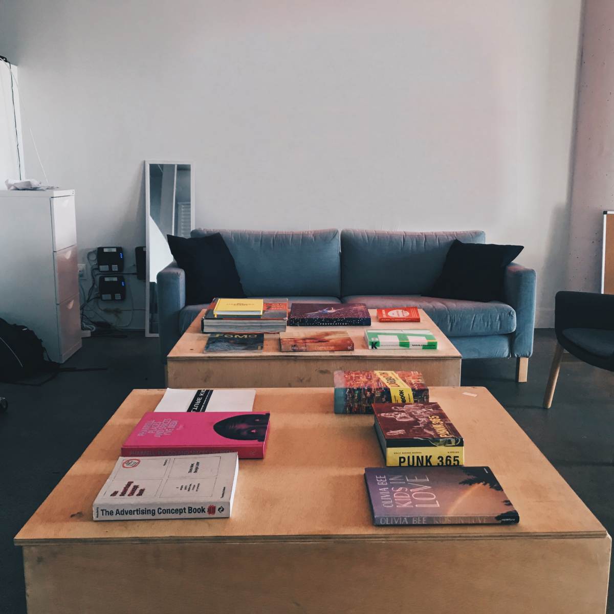A modern interior space features a gray sofa and two black chairs surrounding a wooden coffee table stacked with various books.