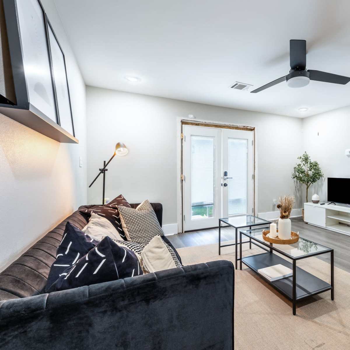 A modern living room with a gray sofa, a glass coffee table, and a view of double French doors leading to an outdoor area.