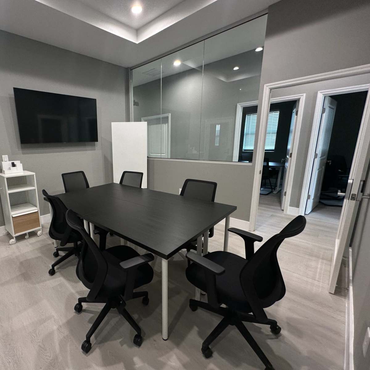 A modern conference room with a large table surrounded by six black chairs and a wall-mounted television.
