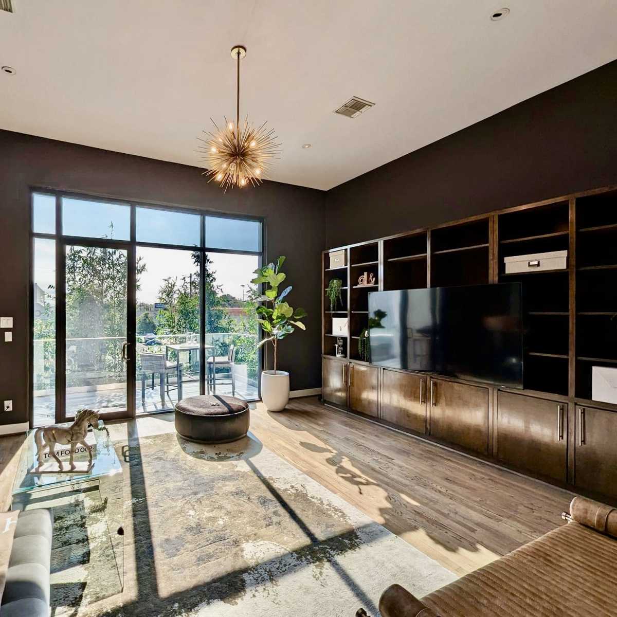 A modern living room with a large window, a sectional sofa, a round ottoman, and a wall-mounted television.